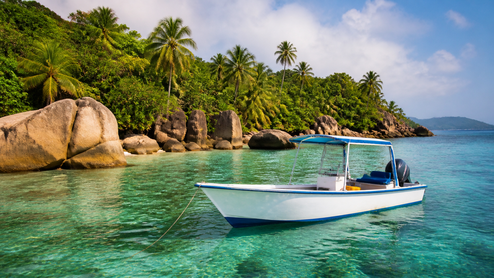Bateau de plongée à l'ancre dans une baie calme de l'archipel des Seychelles, eau turquoise et île granitique au loin