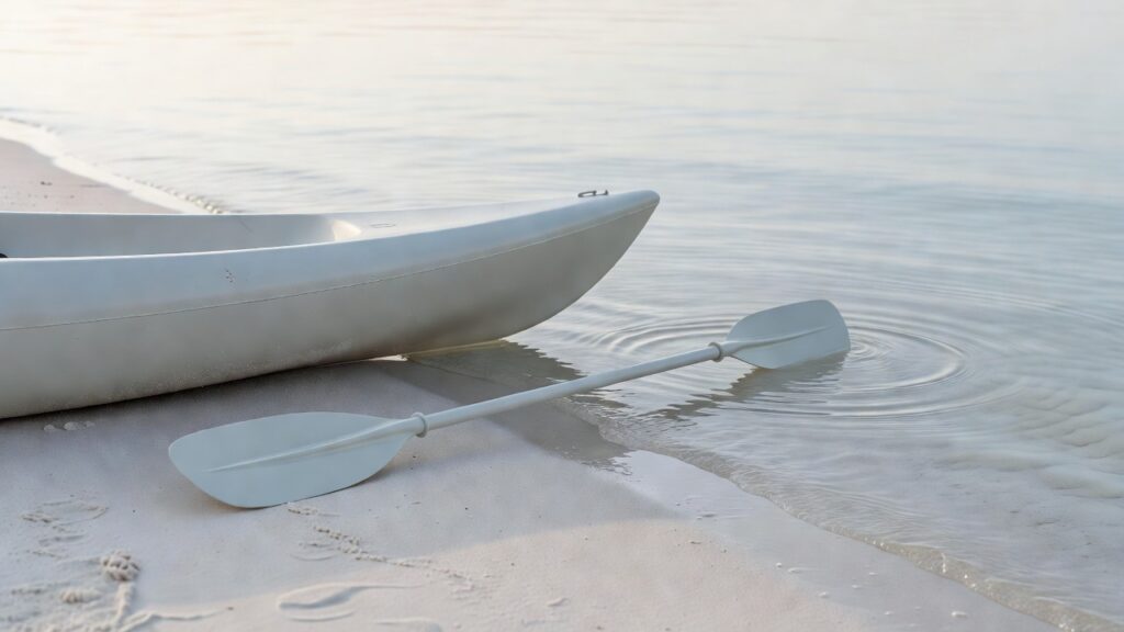 Proue de kayak et pagaie sur le sable, au bord d'une eau calme.